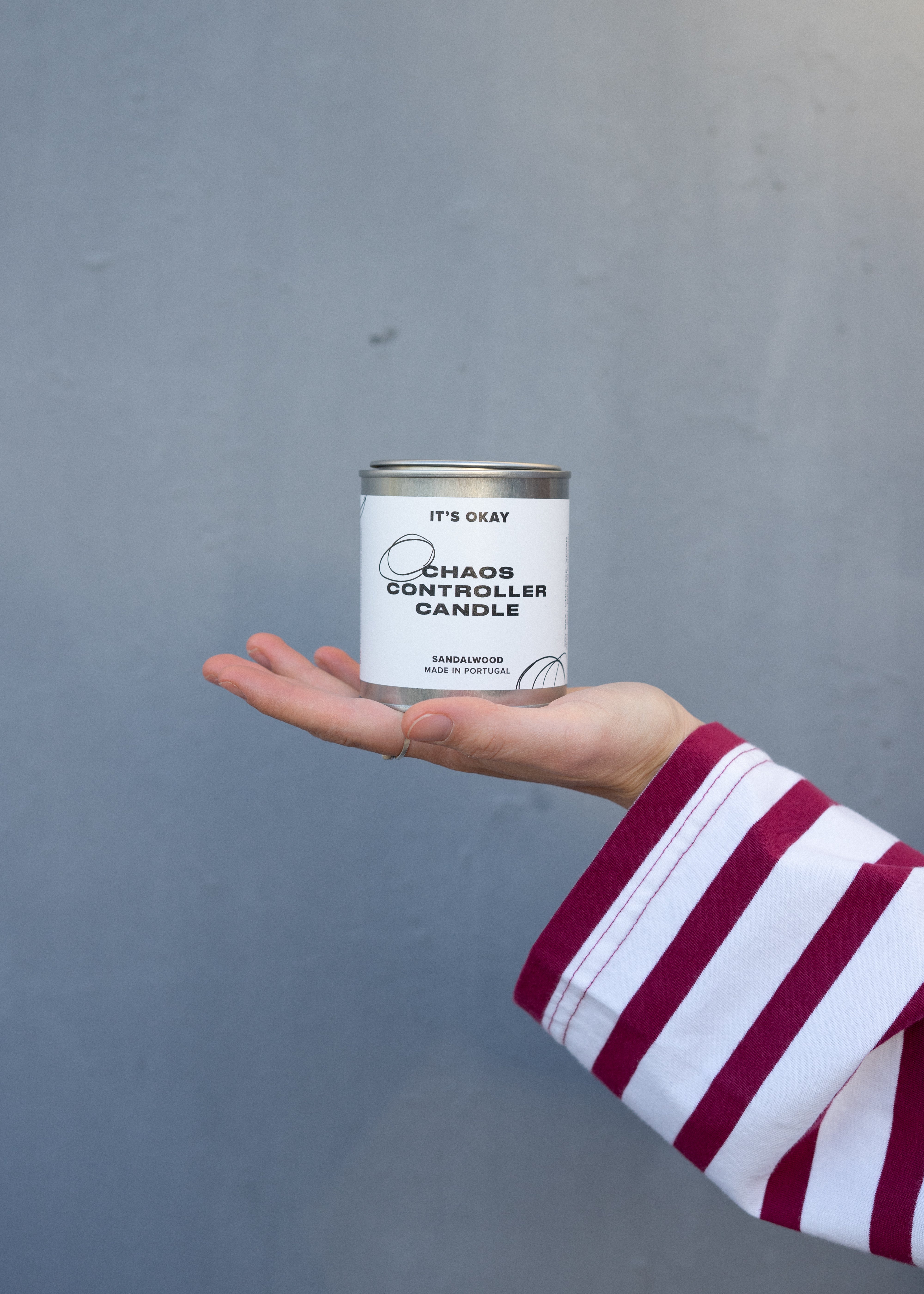 Hand holding a 'Chaos Controller Candle' can against a gray background
