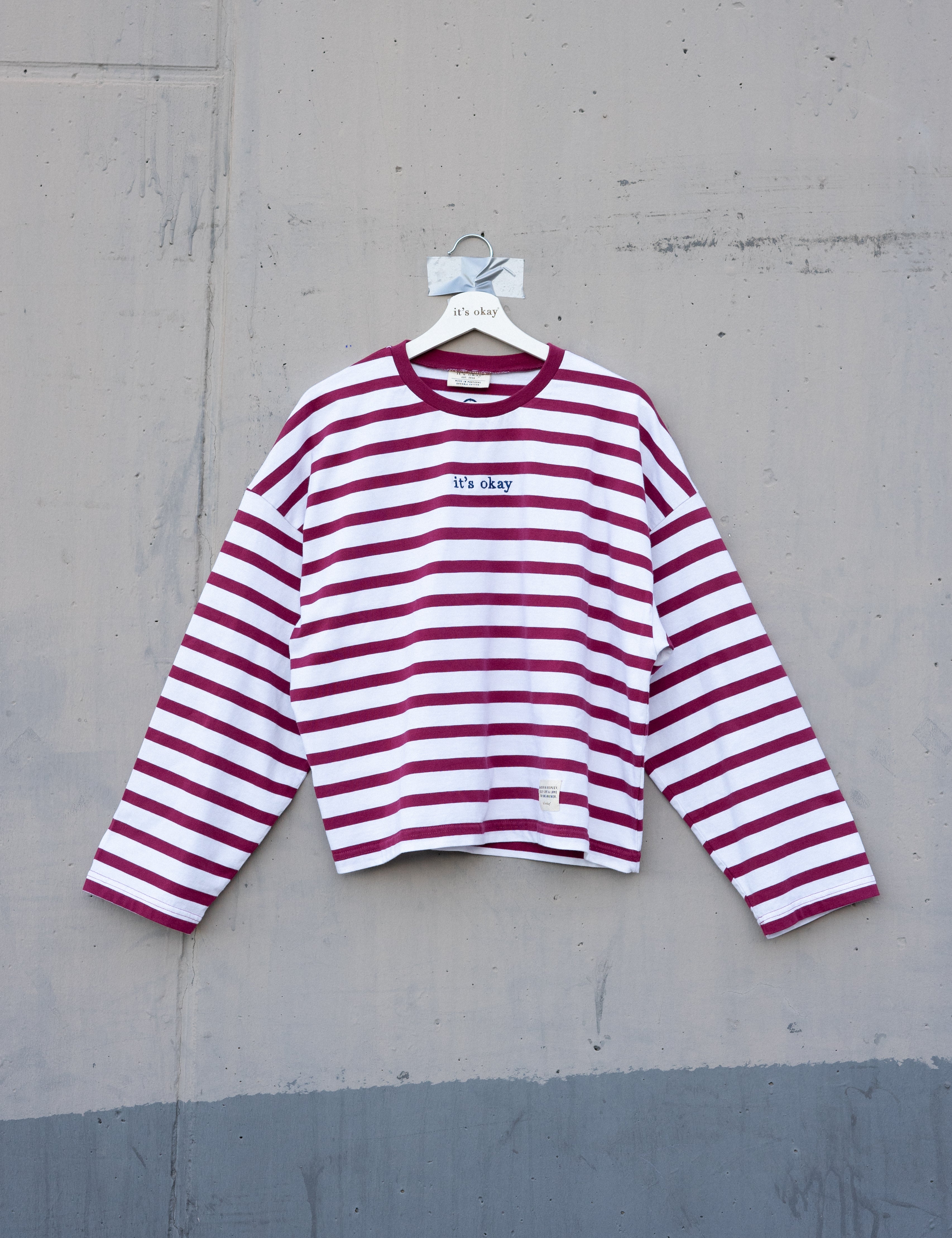 Red and white striped shirt on a hanger against a gray concrete wall.