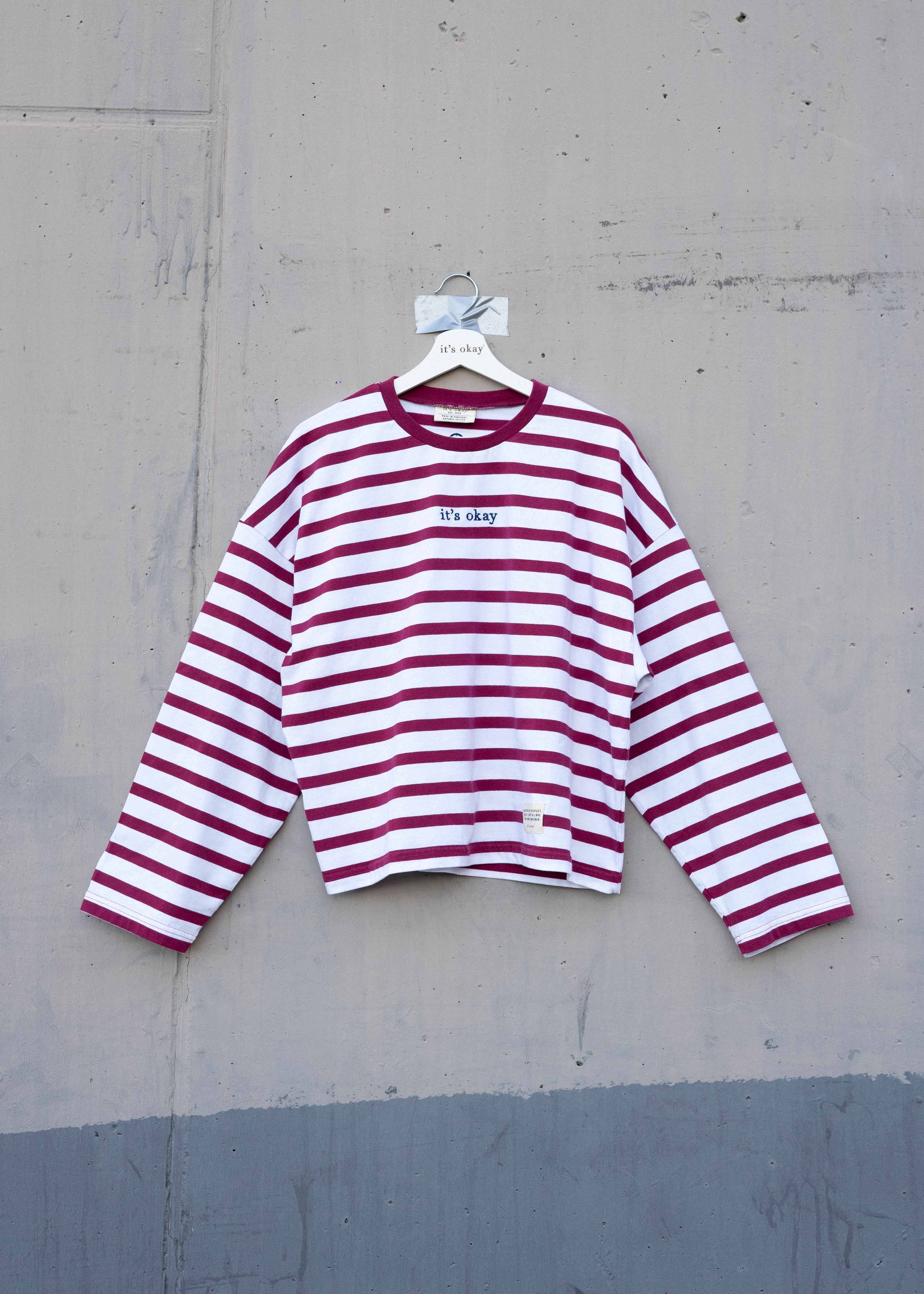 Red and white striped shirt on a hanger against a gray concrete wall.