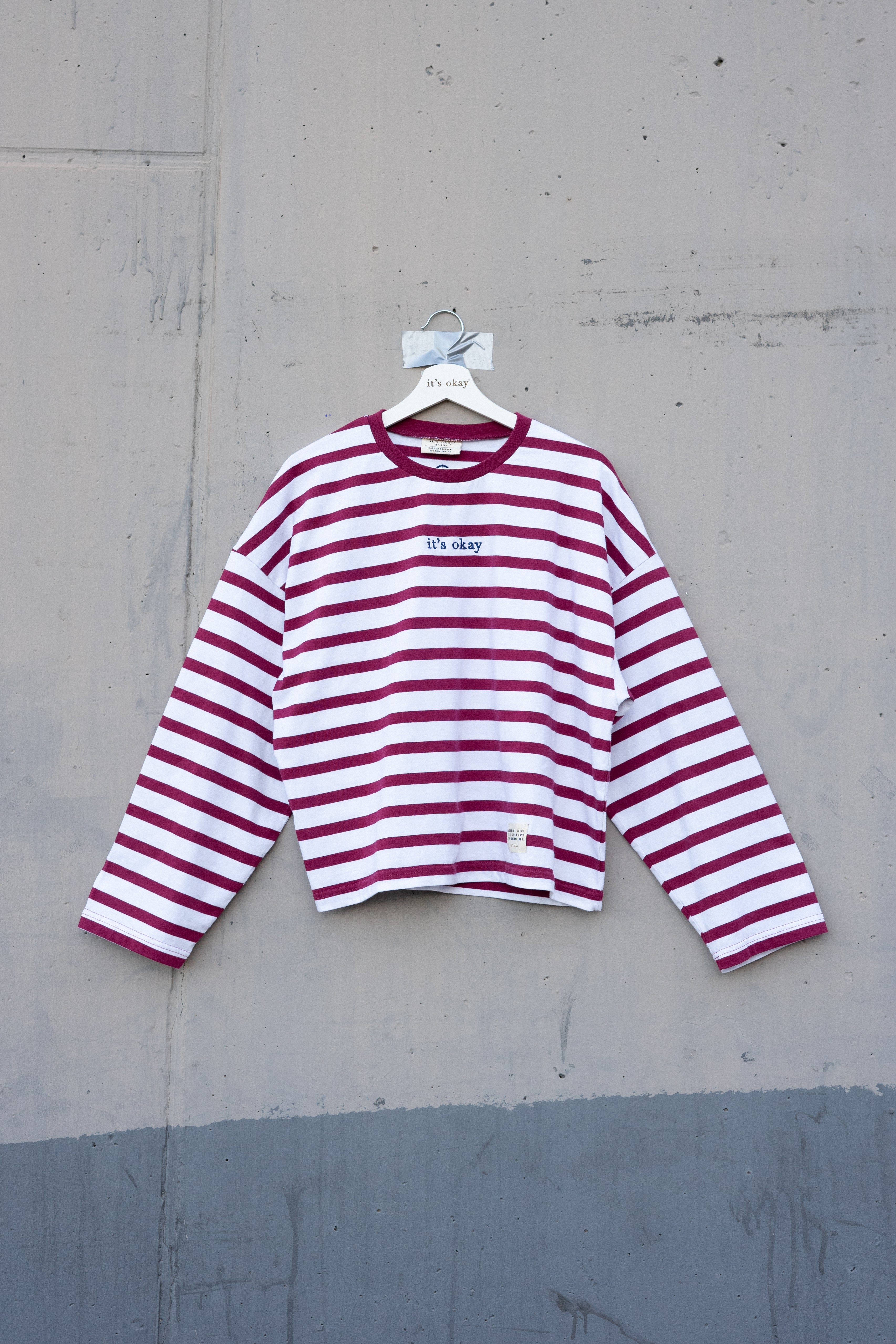 Red and white striped shirt on a hanger against a gray concrete wall.