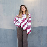 Girl wearing a red and white striped shirt and brown pants standing against a gray wall.
