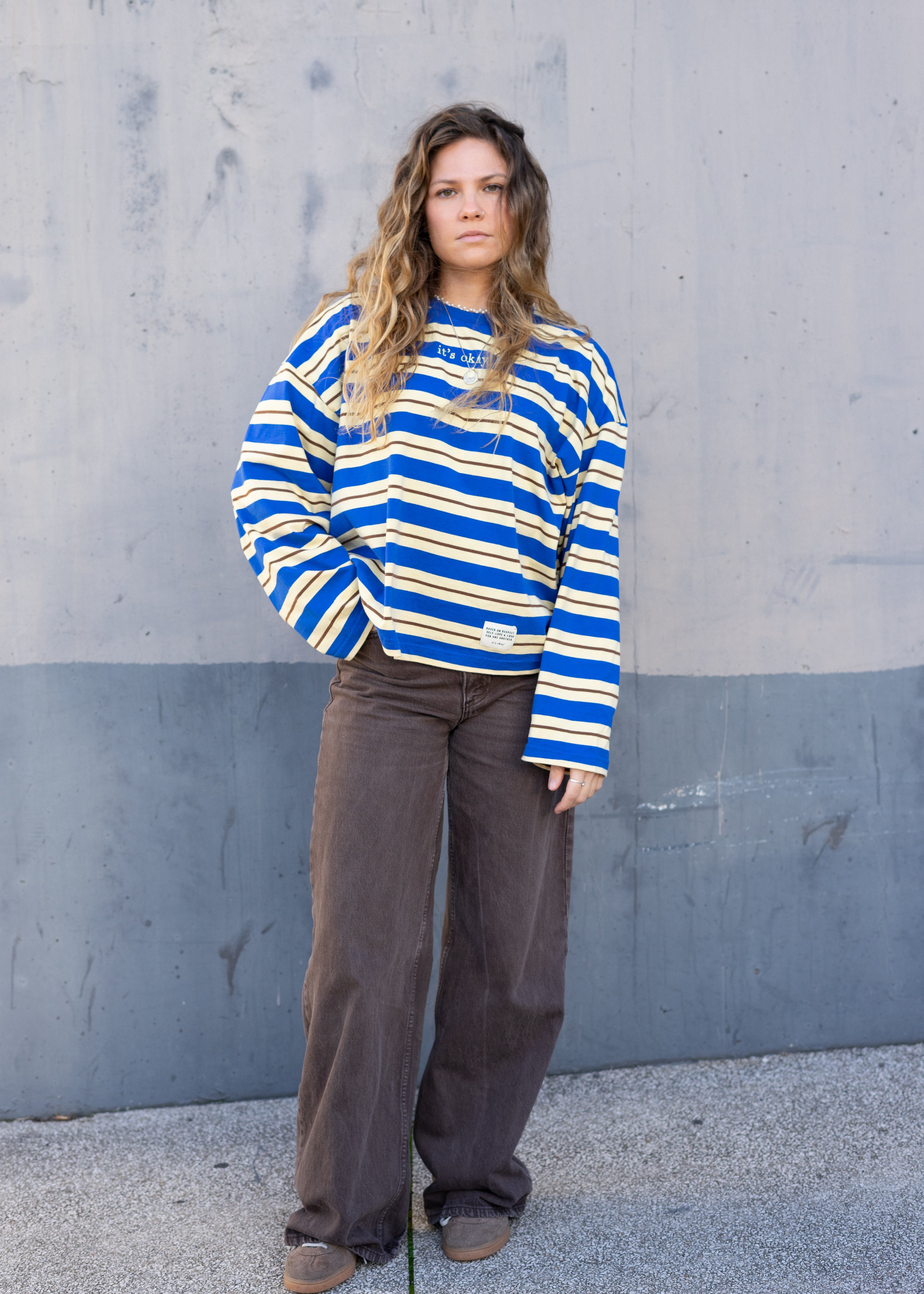 Woman wearing a blue and yellow striped sweater against a gray wall.