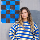 Woman wearing a blue and white striped sweater standing next to a checkered artwork on a gray wall.