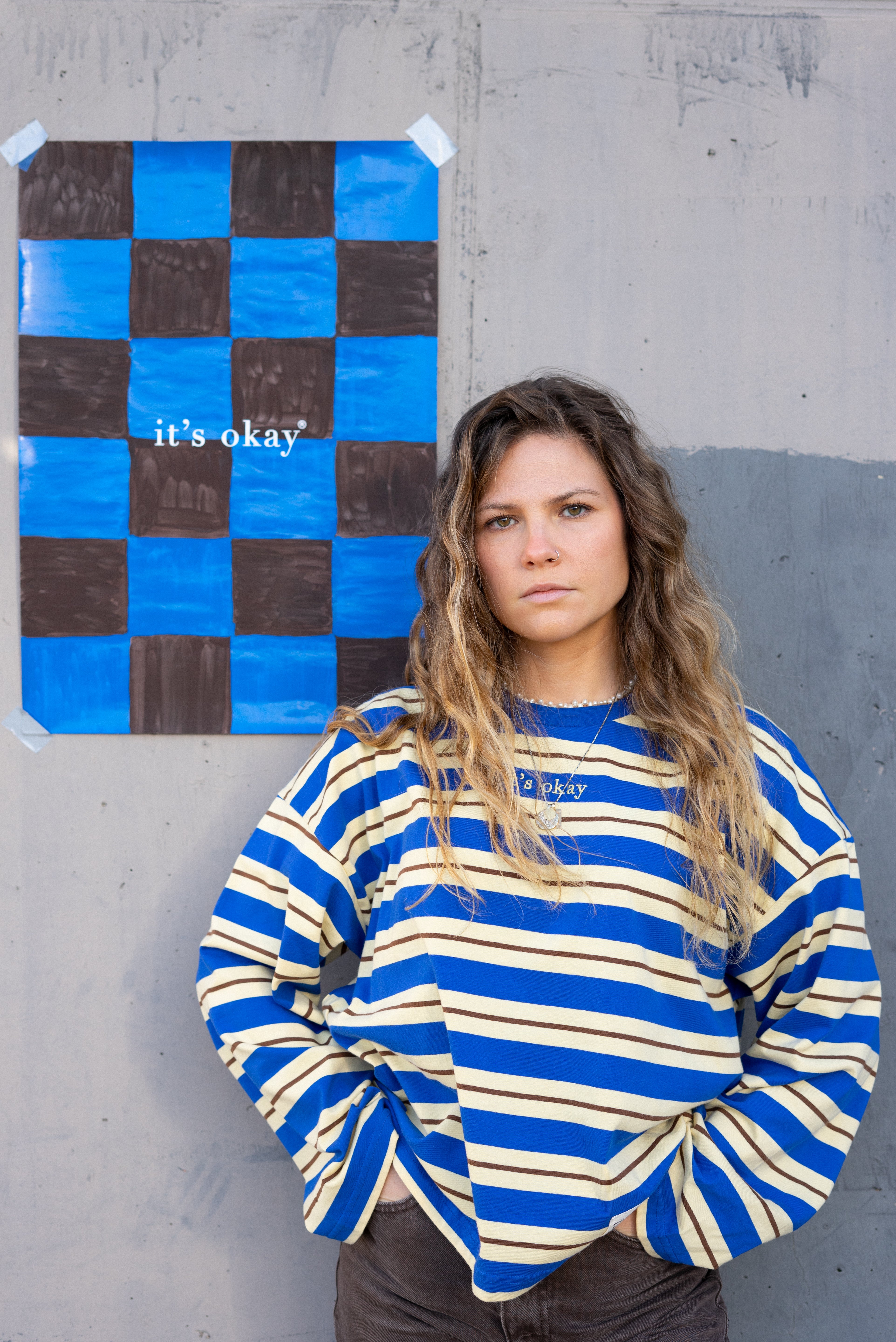 Woman wearing a blue and white striped sweater standing next to a checkered artwork on a gray wall.