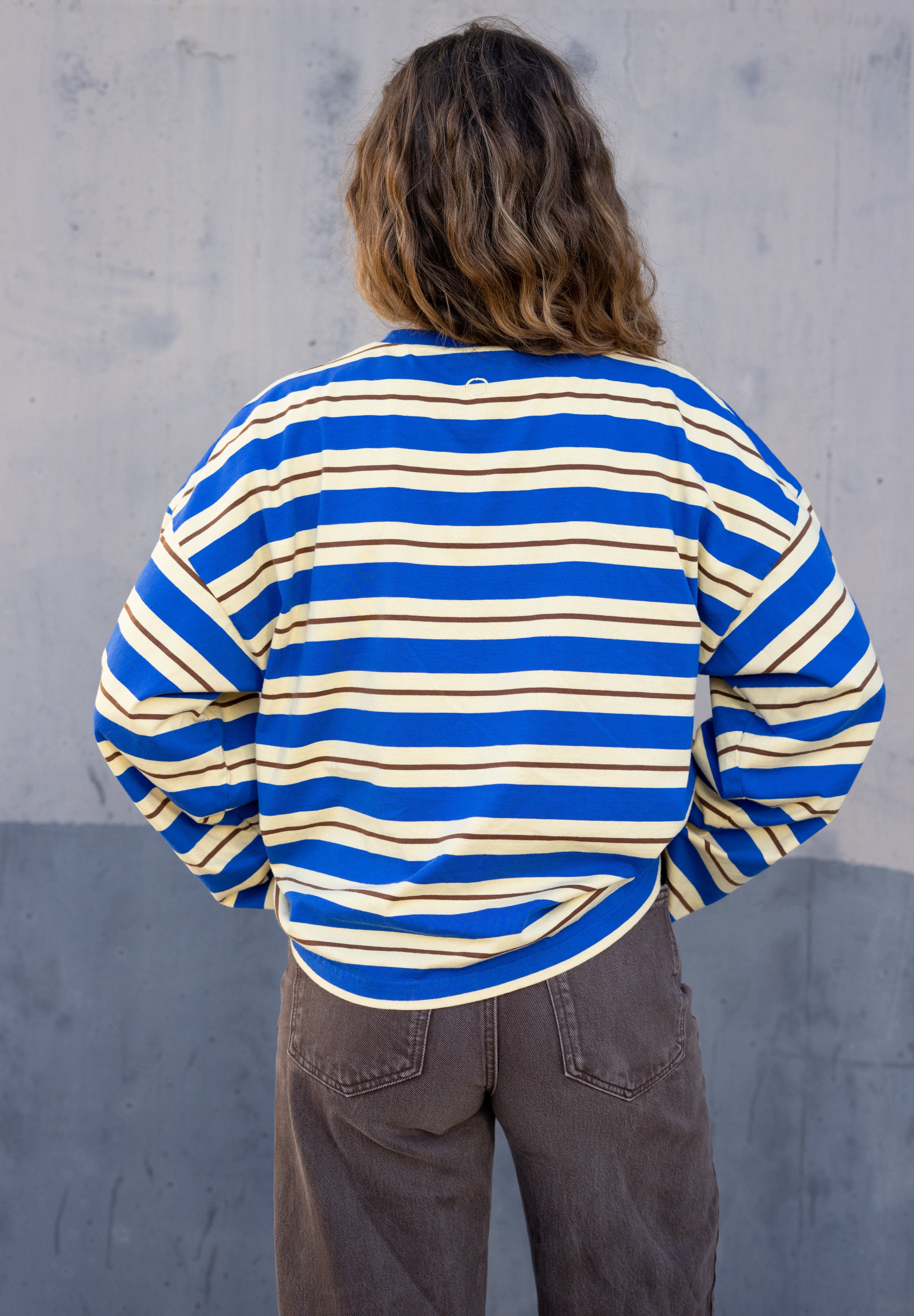 Person wearing a blue and white striped shirt against a gray concrete wall.