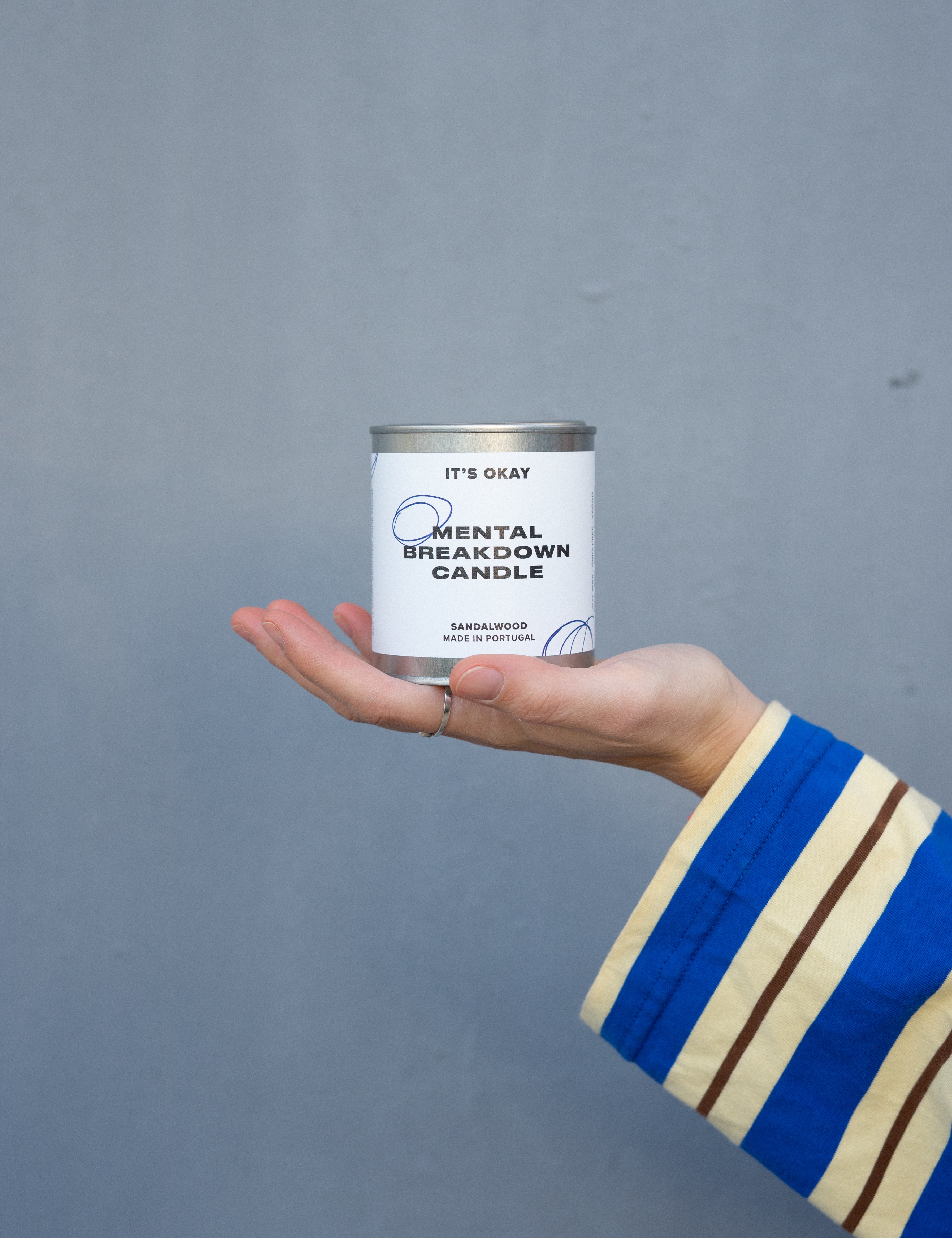 Hand holding a can labeled 'Mental Breakdown Candle' against a gray background