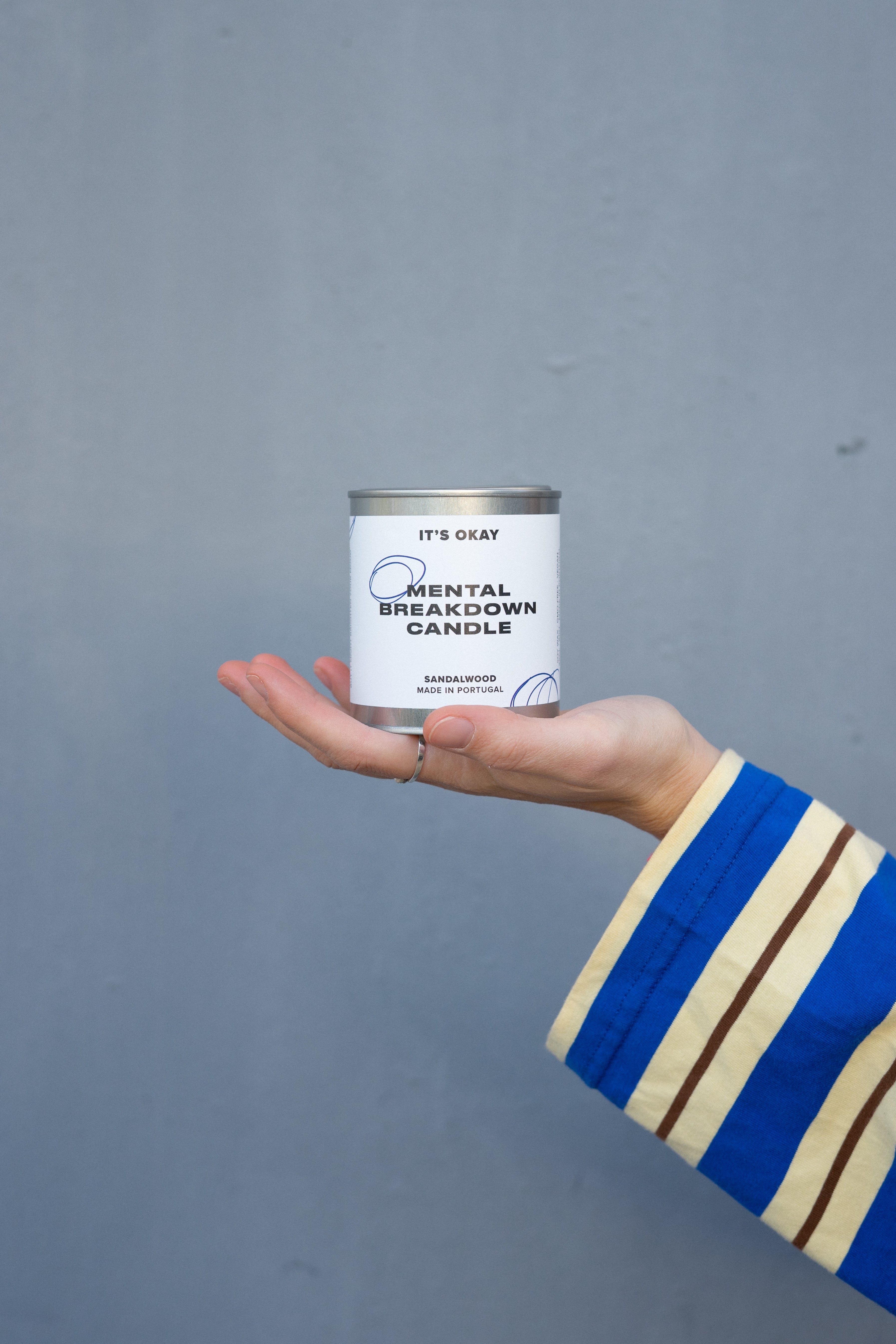 Hand holding a can labeled 'Mental Breakdown Candle' against a gray background
