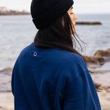 Back view of woman wearing navy IT’S OKAY organic cotton crewneck with embroidered circle, outdoors by the sea.