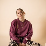 Model seated wearing burgundy IT’S OKAY organic cotton crewneck bordeaux, relaxed fit.