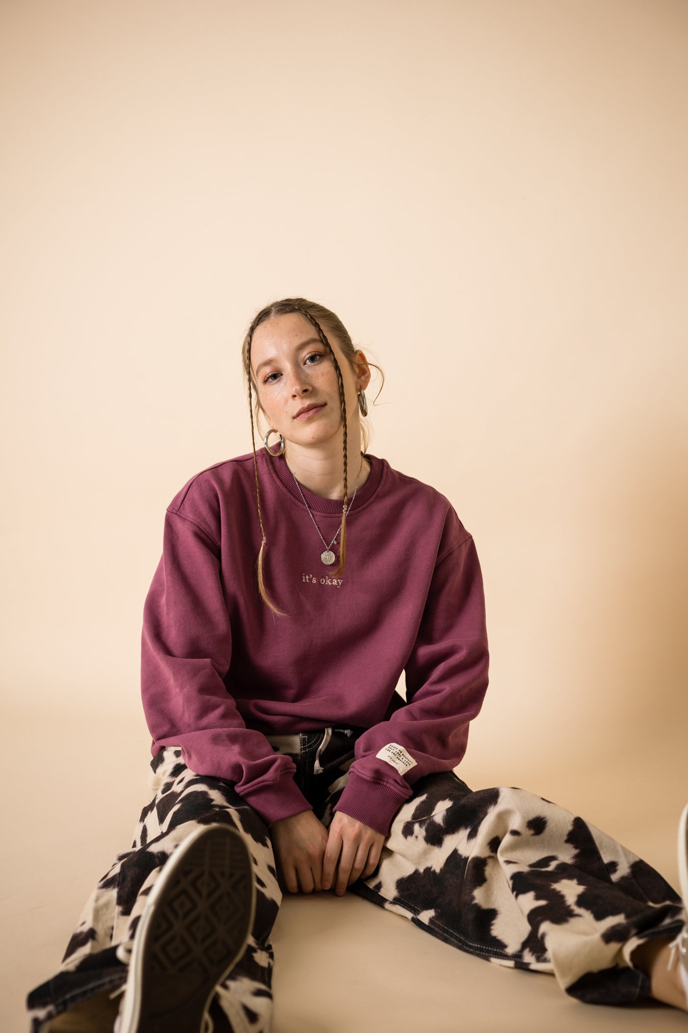 Model seated wearing burgundy IT’S OKAY organic cotton crewneck bordeaux, relaxed fit.