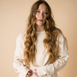 blond girl with blue eyes wearing an organic crew neck sweater in off-white, seamless design. Relaxed and minimal style, perfect for any occasion. Studio Photography gender neutral apparel
