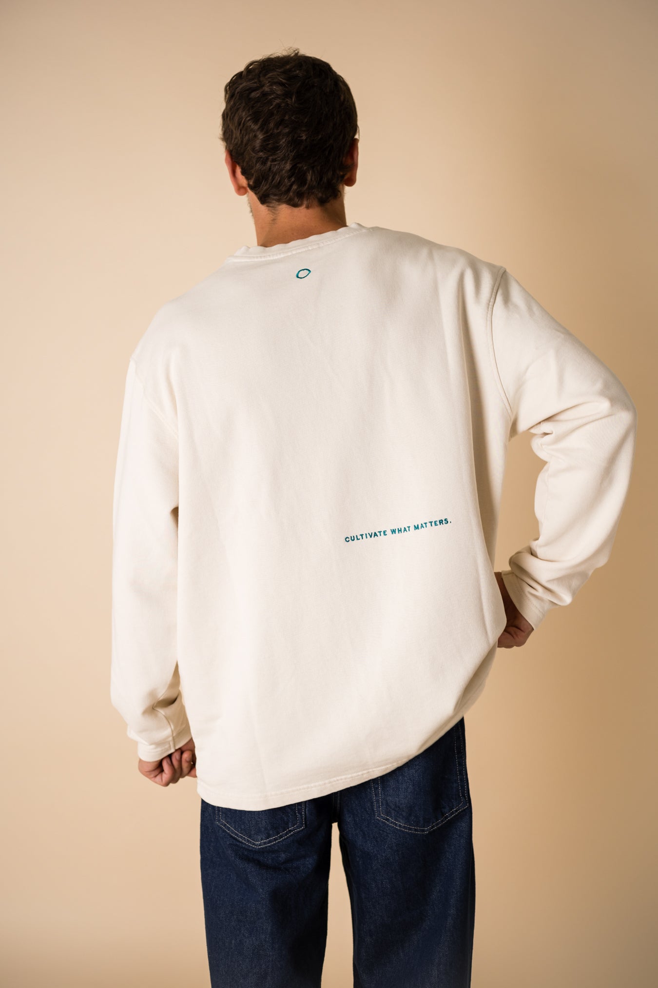 Man's back wearing an organic crew neck sweater in off-white, seamless design. Relaxed and minimal style, perfect for any occasion. You can read the embroidery: Cultivate what matters Studio Photography gender neutral apparel.