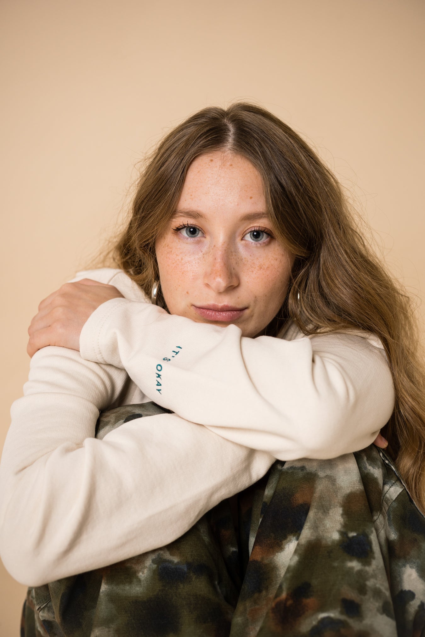 Blond girl wearing an organic crew neck sweater in off-white, seamless design. Relaxed and minimal style, perfect for any occasion. Studio Photography gender neutral apparel. close up of the face and embroidery: Cultivate what matters